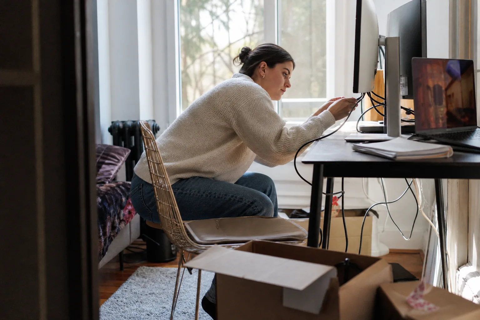 Person setting up a second monitor on a small desk with cables and a box on the floor